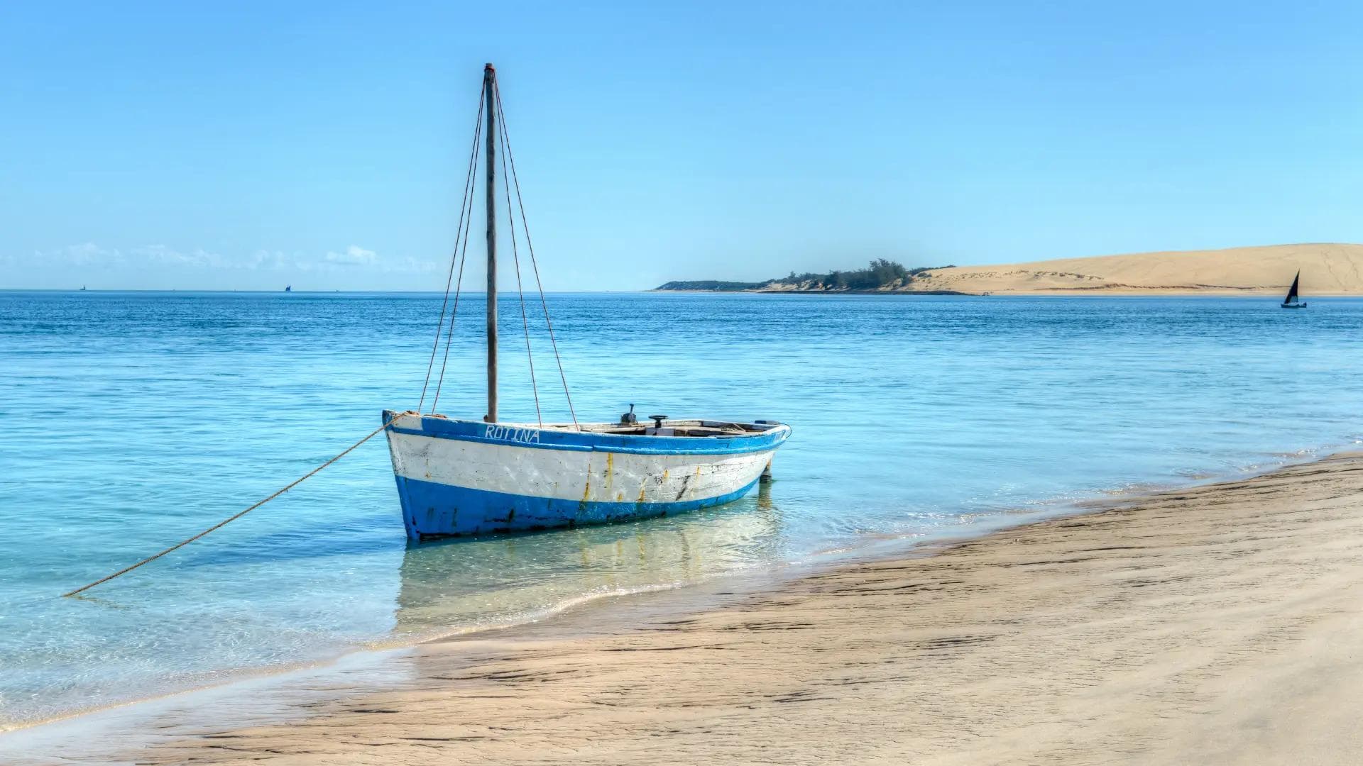 Traditional dhow anchored in shallow turquoise water along a sandy beach in Mozambique