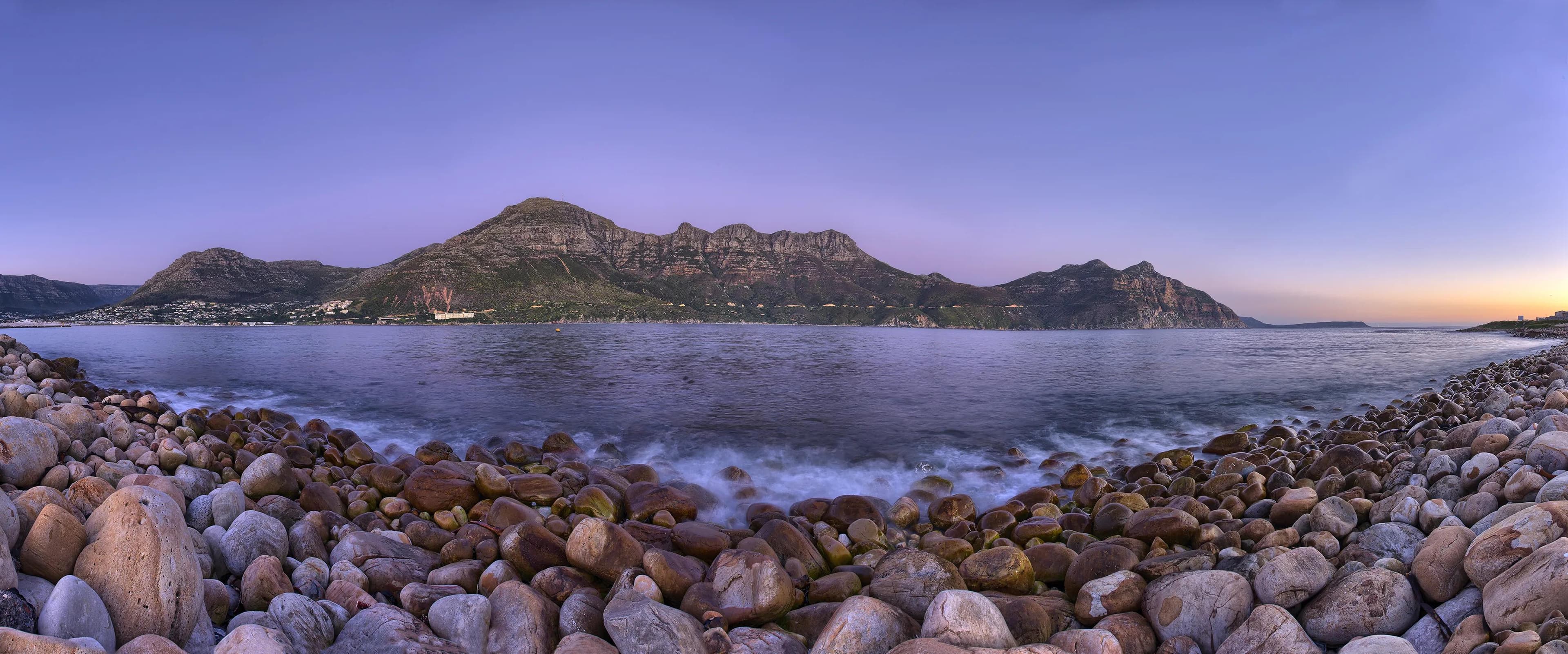 Rocky shoreline with panoramic view of Cape Town’s coastal mountains at sunset
