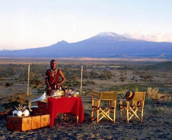 Maasai host standing beside a luxury breakfast setup with Mount Kilimanjaro in the background