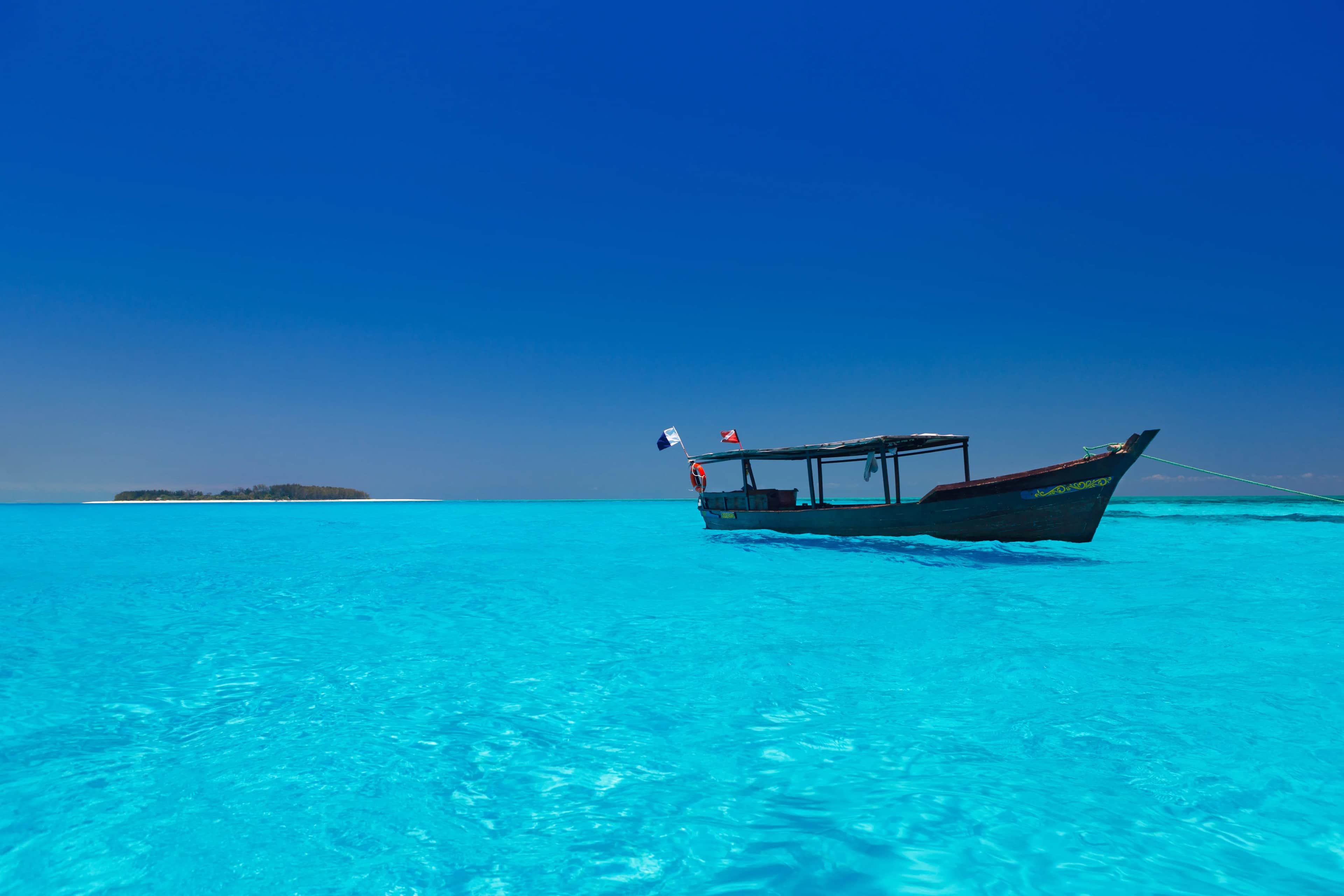 Traditional dhow floating on crystal-clear turquoise waters under a deep blue sky at Diani Beach, Kenya
