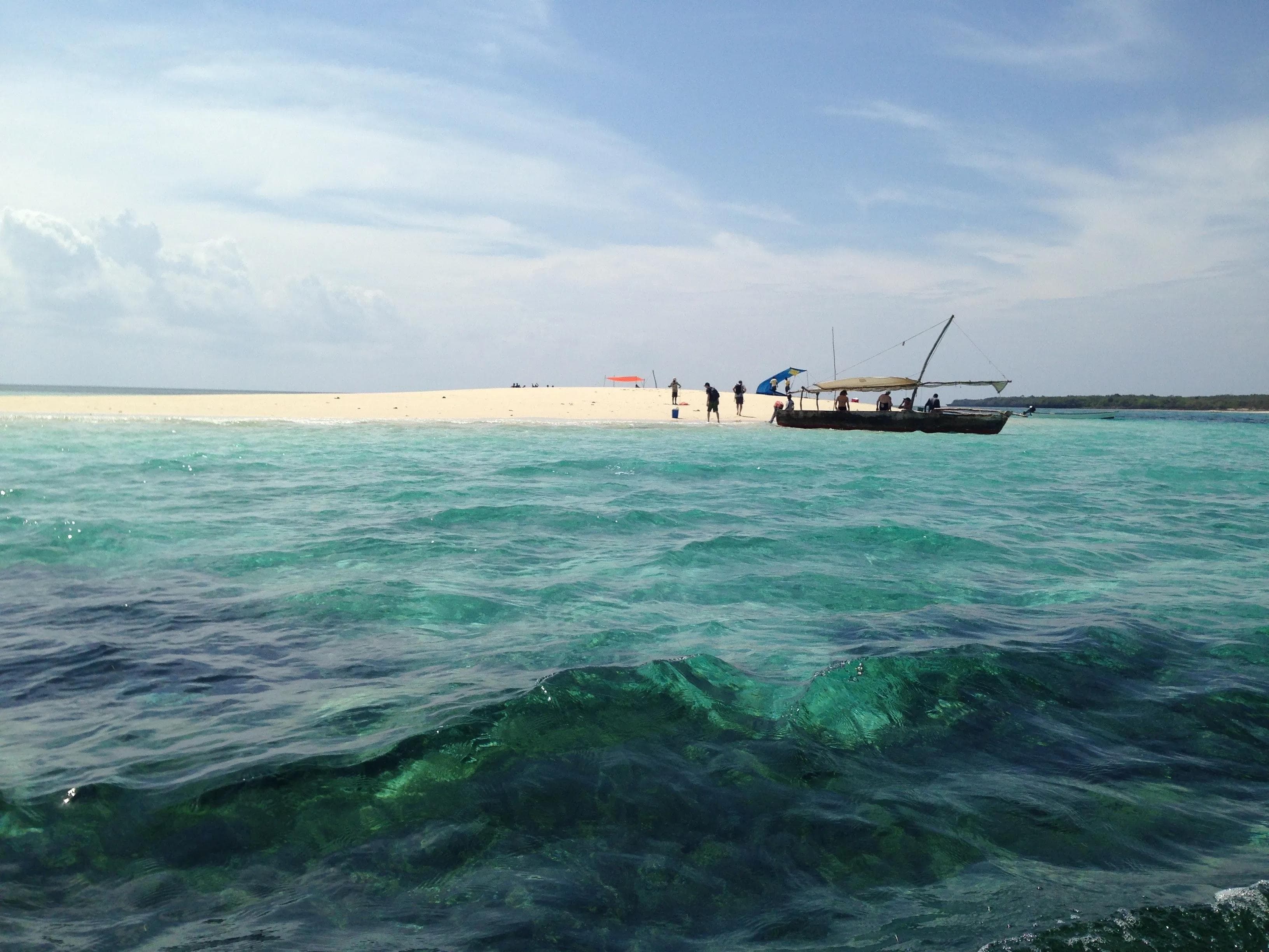 Traditional dhow boat anchored near a white sandbar in the clear turquoise waters of Zanzibar