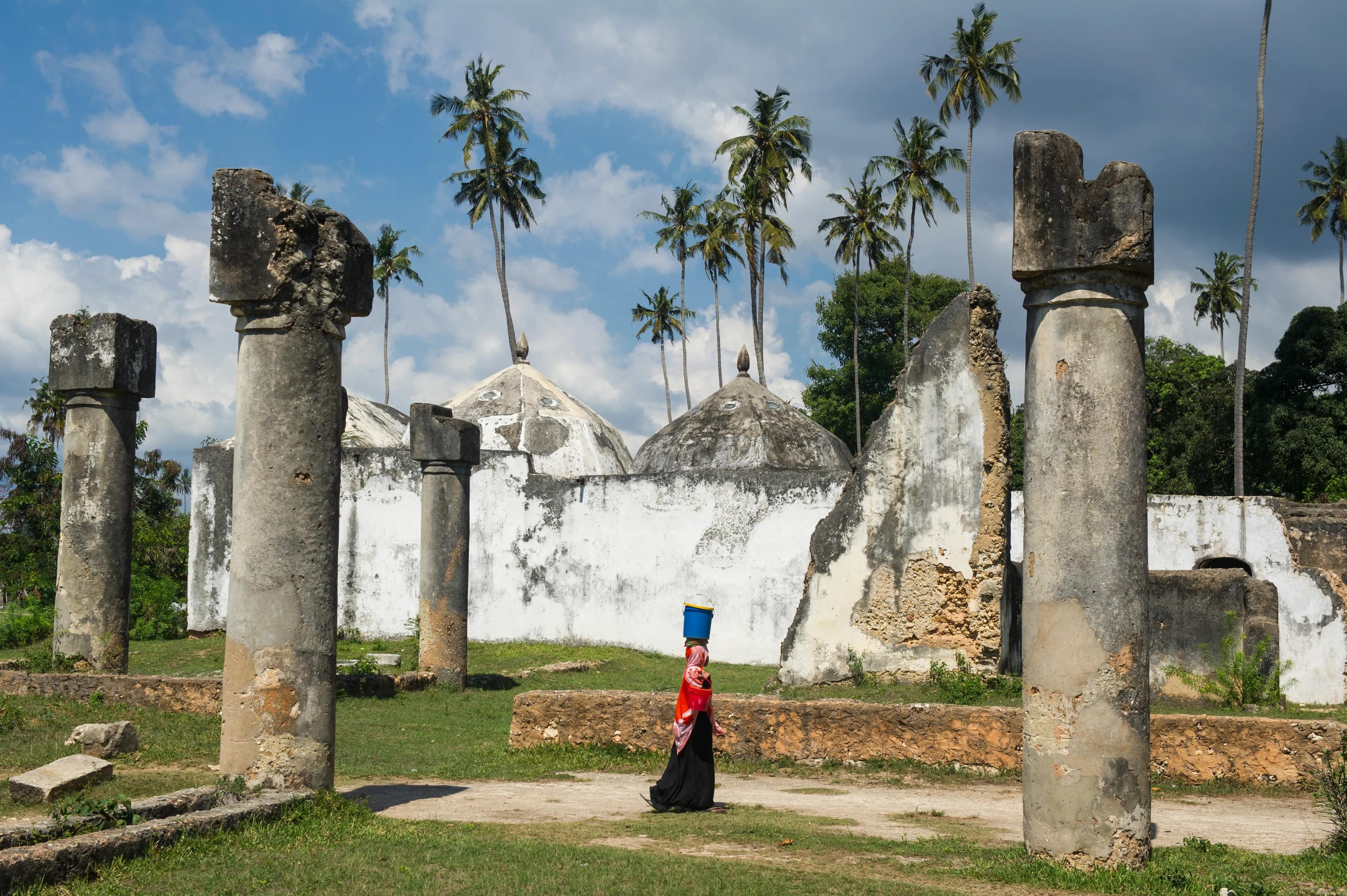 Woman in traditional dress walking through ancient Swahili ruins with palm trees in Tanzania